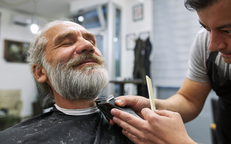 A barber carefully trims a clients gray beard in a modern barber salon.