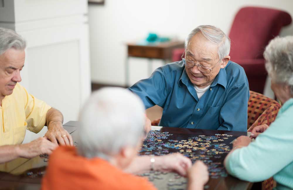 Group of elderly people joyfully working together on a jigsaw puzzle at a table.