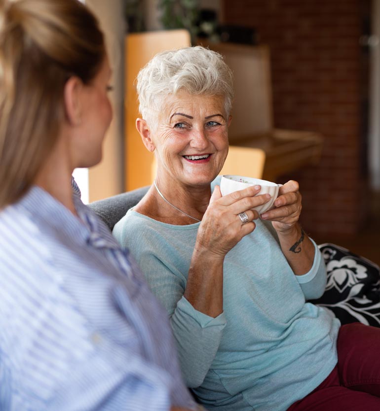 Smiling senior woman holding a cup, engaged in a pleasant conversation with a younger team member.